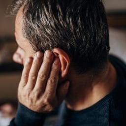 Man rubbing ear from earwax buildup.