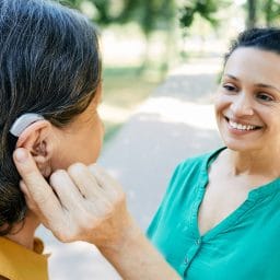 Woman wearing a hearing aid chatting with her friend outdoors.